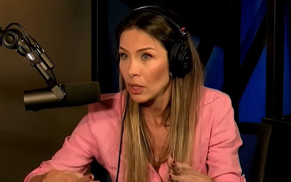 Lizi está olhando para frente, veste camiseta rosa e fala perto de um microfone
