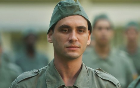 Guilherme Prates com roupa verde de soldado em cena como Lorenzo na novela Além da Ilusão