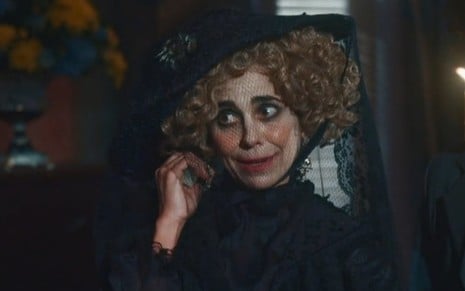 Paula Cohen grava cena como Lota em Nos Tempos do Imperador; atriz está com uma das mãos na orelha e expressão confusa