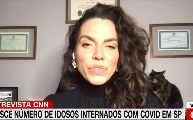 Luana Araújo concedendo uma entrevista, enquanto seu gato se posiciona atrás dela