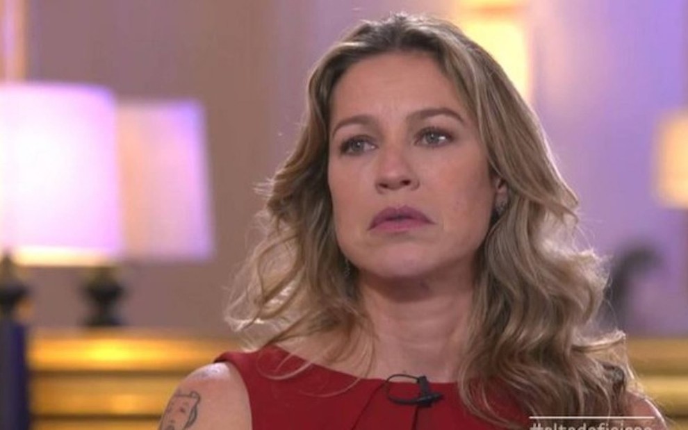 A atriz Luana Piovani usa camia vermelha regata e olha com tristeza para frente durante entrevista a um programa da TV portuguesa