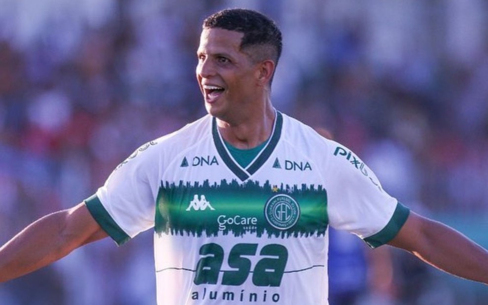 Lucão do Break, do Guarani, comemora gol de braços abertos vestindo uniforme branco com faixa verde no peito