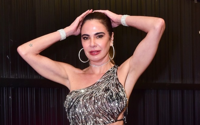 Luciana Gimenez está com top brilhoso, cabelos presos para traz e mãos apoiadas na cabeça