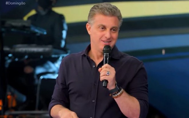 Luciano Huck com uma camisa azul no cenário do Domingão com Huck
