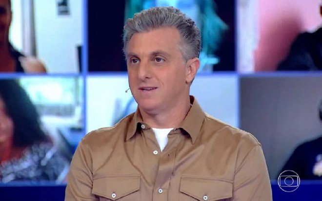 Luciano Huck com uma camisa marrom no cenário do Domingão com Huck