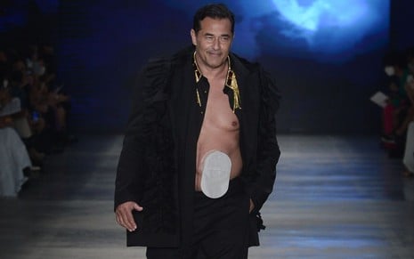 Luciano Szafir usa um conjunto preto e desfil com bolsa de estomia à mostra