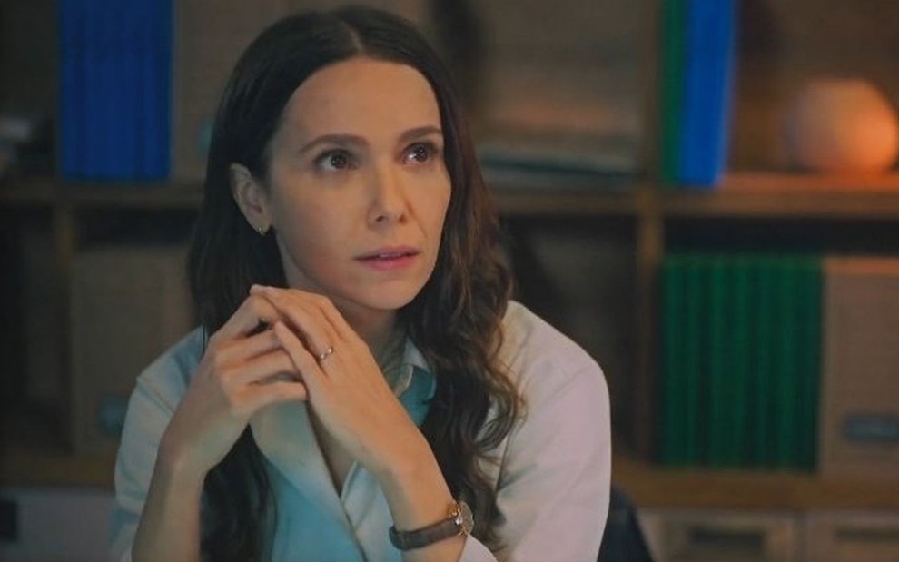 Em cena de Terra e Paixão, Lucinda (Débora Falabella) está sentada em frente a sua mesa de trabalho, olhando para alguém