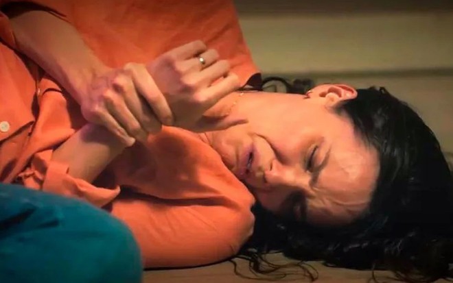 Em cena de Terra e Paixão, Débora Falabella está caída no chão segurando um dos pulsos que está machucado