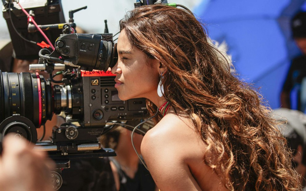Caracterizada como sua personagem em Travessia, Lucy Alves observa algo pela câmera de direção