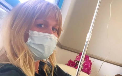 A atriz Ludmila Dayer de máscara, olhando para câmera, em sala de hospital