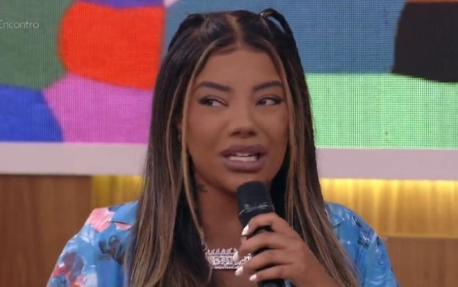 Ludmilla no estúdio do Encontro, ela veste uma camisa azul florida e exibe um semblante de nojo