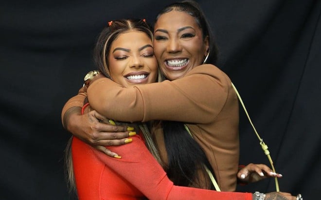 Ludmilla e a mãe, Silvana, se abraçam, sorridentes: a cantora usa um vestido vermelho e mãe um marrom