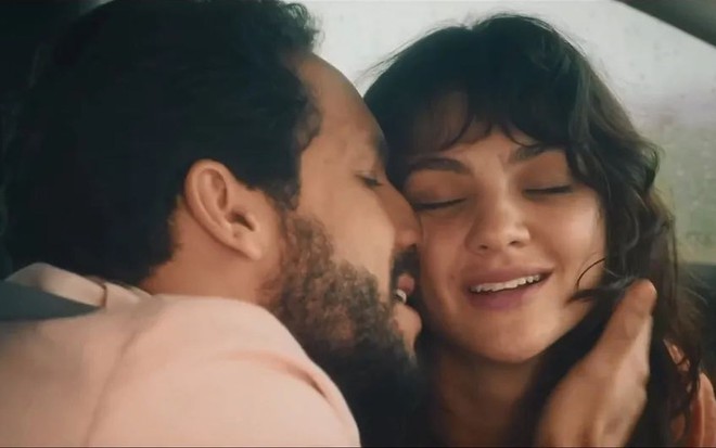 Em cena de Terra e Paixão, Rainer Cadete está beijando o rosto de Debora Ozório dentro de um carro