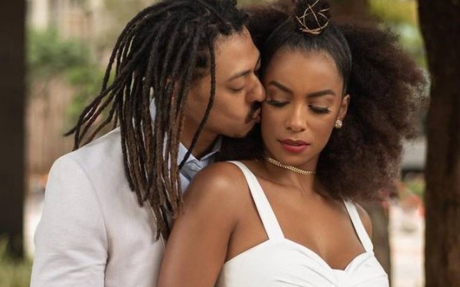 Luis Navarro e Ivi Pizzott, ambos de roupas brancas de festa, ele beija a bochecha dela