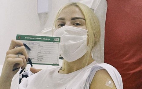 Luísa Sonza de máscara e com o cartão de vacinação da prefeitura de São Paulo após tomar vacina