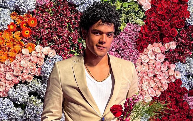 Luiz Fortes de terno bege em frente a um painel de flores