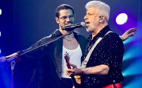 De óculos, José Loreto está no palco cantando com Lulu Santos