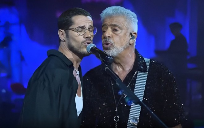 De óculos, José Loreto está no palco cantando com Lulu Santos