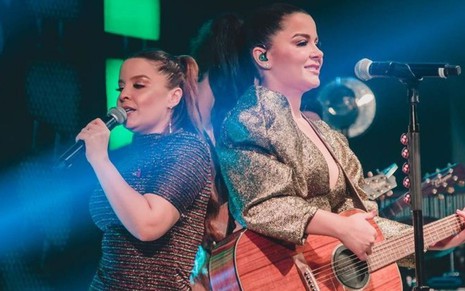 Imagem de Maiara cantando (à esq.) e Maraisa tocando violão durante show