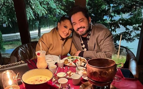 Os cantores Maiara e Fernando Zor; eles estão agasalhados e sentados a uma mesa servida de fondue