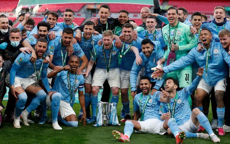 Jogadores do Manchester City usam o uniforme com camisa azul e short branco e comemorando o título do Campeonato Inglês da temporada 2020/2021