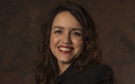Manuela Dias com uma roupa preta e um sorriso em uma foto de divulgação da Globo