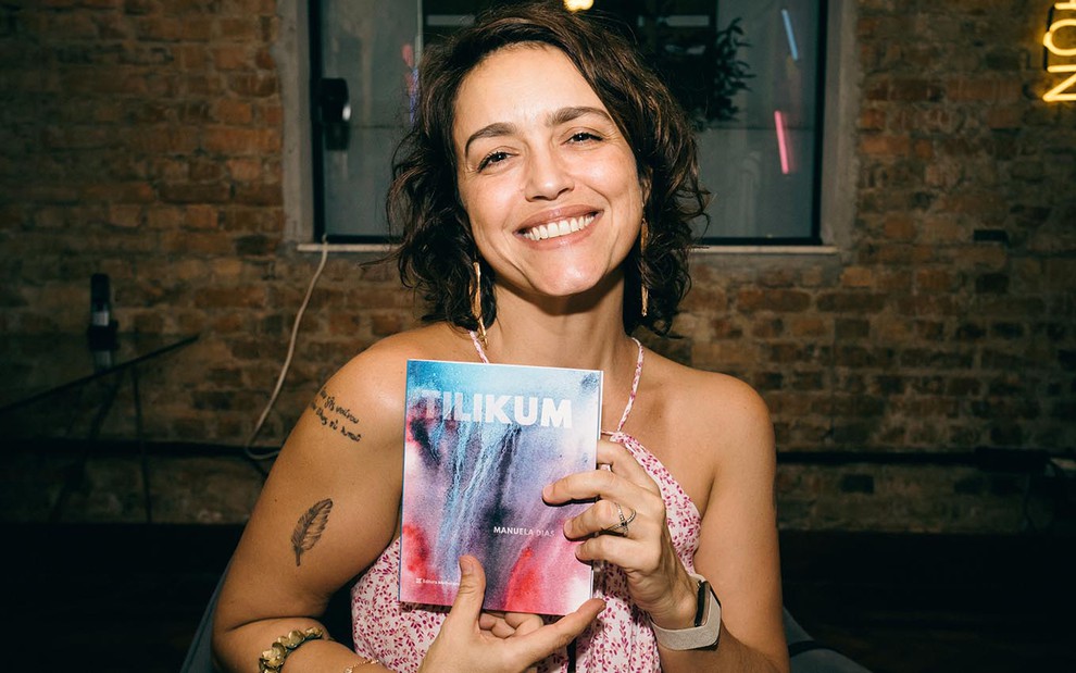 A autora Manuela Dias segura um livro com o título Tilikum em uma noite de autógrafos