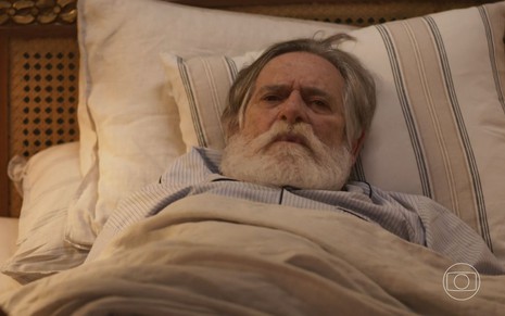 O ator José de Abreu como o coronel Tertúlio em Mar do Sertão; ele está deitado, com a cabeça encostada no travesseiro, olhando para frente com cara de assustado