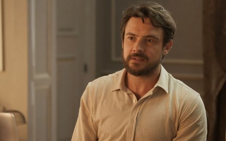O ator Sergio Guizé como Zé Paulino/José em Mar do Sertão; ele está sentado de lado, olhando para a frente com cara séria