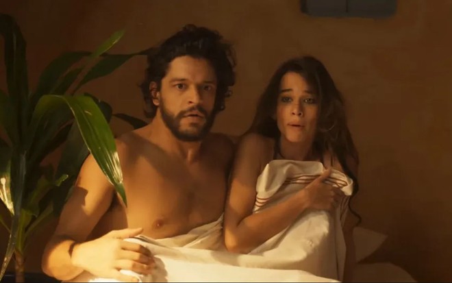Os atores Pedro Lamin e Theresa Fonseca como Maruan e Labibe em Mar do Sertão; eles estão deitados em uma cama e cobertos com um lençol até a altura do peito enquanto olham para frente com cara de espantados