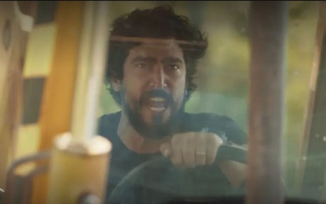O ator Renato Góes como Tertulinho em Mar do Sertão; ele está sentado atrás de um volante, dirigindo um trator e olhando para frente enquanto grita com cara de furioso