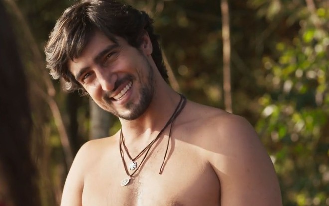 O ator Renato Góes como Tertulinho em Mar do Sertão; ele está sem camisa, com a cabeça inclinada para o lado olhando para a frente e sorrindo