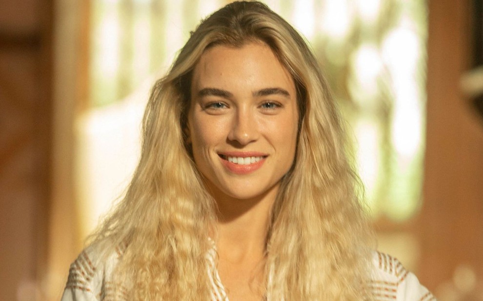 Marcela Fetter com os cabelos loiros soltos e sorrindo caracterizada como Érica, personagem de Pantanal
