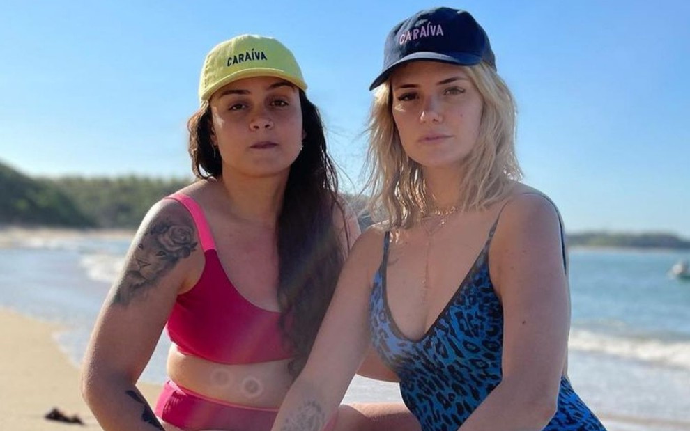 Marcela Mc Gowan e Luiza em foto publicada no Instagram; as duas estão agachadas na praia e de boné, Marcela veste um maiô azul e Luiza um biquíni vermelho