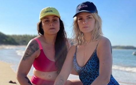 Marcela Mc Gowan e Luiza em foto publicada no Instagram; as duas estão agachadas na praia e de boné, Marcela veste um maiô azul e Luiza um biquíni vermelho