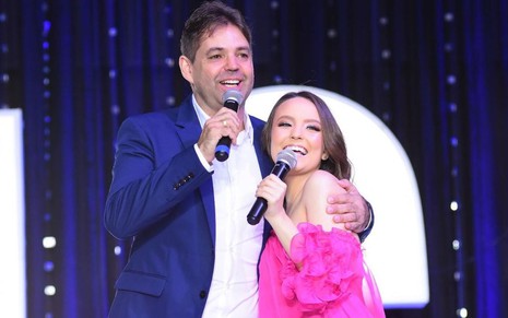 O empresário Marcelo Germano ao lado de Larissa Manoela, ambos com microfones nas mãos, em palco, abraçados