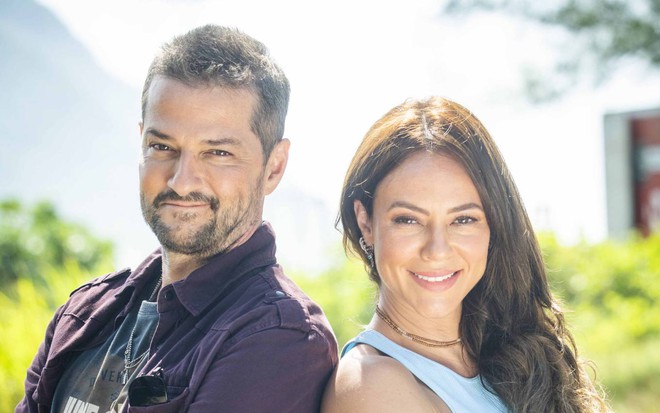Ator Marcelo Serrado e Paolla Oliveira ficar de costas um para o outro e sorriem para a câmera