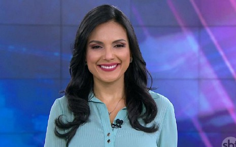 Márcia Dantas usa uma blusa azul e sorri durante uma chamada do SBT Brasil, principal telejornal do SBT