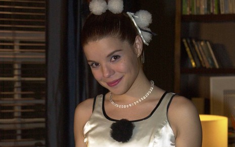 A atriz Pitty Webo em cena como Marcinha em Mulheres Apaixonadas (2003), cm leve sorriso de boca fechada, colar e tiara brancos