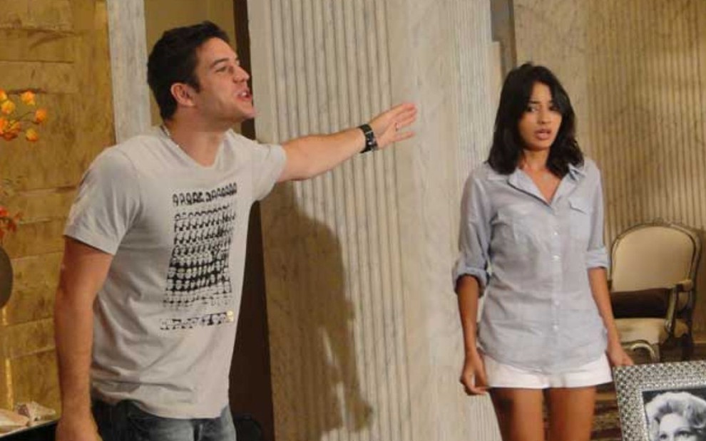 Marco Pigossi aponta para Carolina Oliveira, que está com expressão de choro, em cena da novela Ti Ti Ti