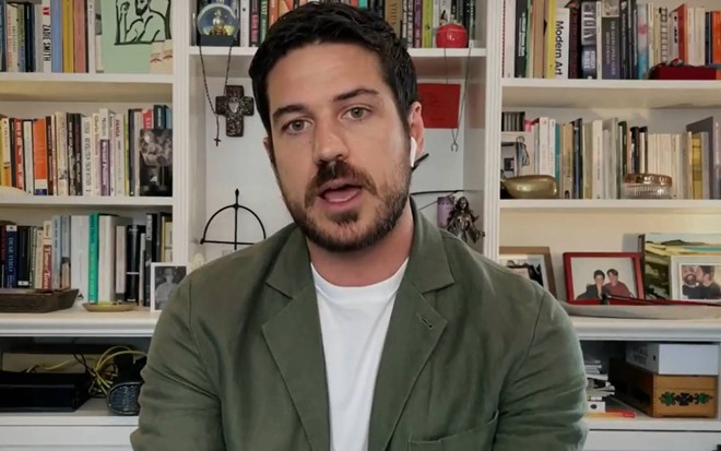 Marco Pigossi em frente a uma estante de livros