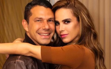Marcos Buaiz encara a câmera com um sorriso; Wanessa Camargo, séria, abraça o então marido pelo pescoço