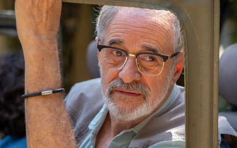 Em cena de Travessia, Marcos Caruso está na janela de um veículo tipo jipe. Ele usa óculos e barba