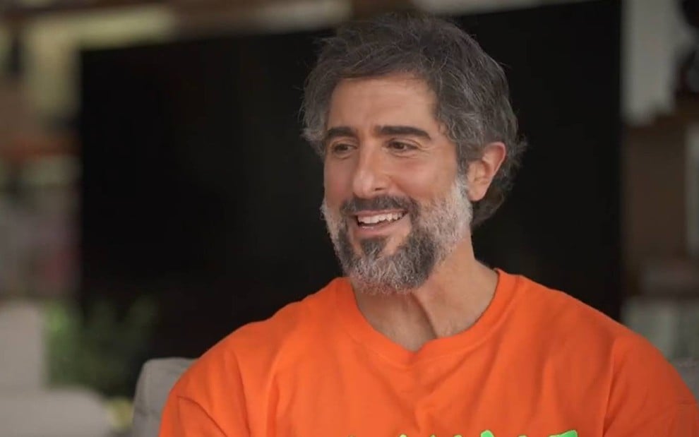 O apresentador Marcos Mion com uma camisa laranja em entrevista ao Fantástico