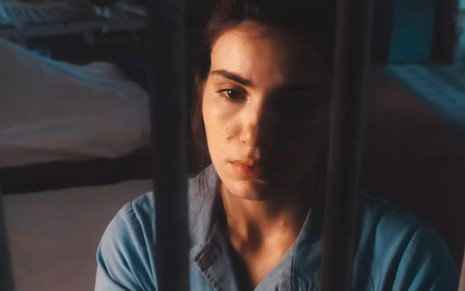 A atriz Camila Queiroz atrás das grades, com expressão triste em cena de Amor Perfeito