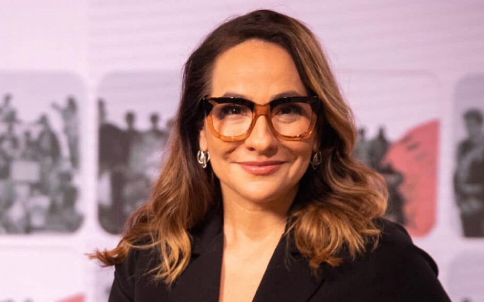 Maria Beltrão com uma blusa preta, óculos e um sorriso no rosto durante uma cobertura na GloboNews