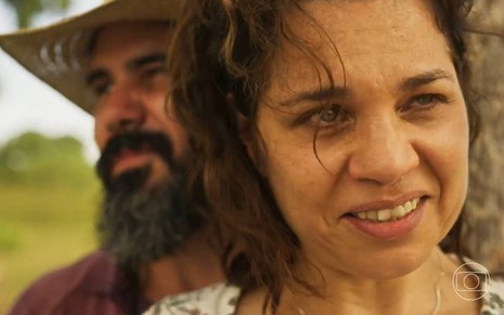 O ator Juliano Cazarré aparece ao fundo de cena de Pantanal na qual Isabel Teixeira está em close com um sorriso malicioso