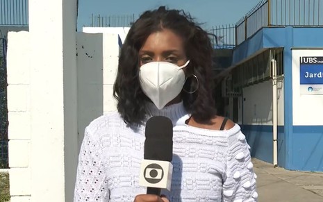 Mariana Aldano de máscara branca e segurando microfone da Globo no SP1 deste sábado (26)