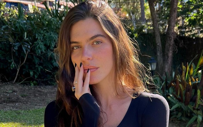 Mariana Goldfarb está sem expressão, com mão apoiada no rosto