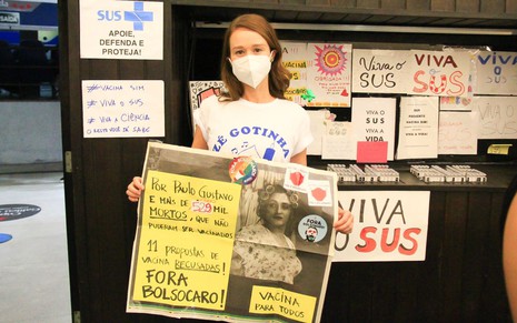 Mariana Ximenes de camiseta branca com desenho do Zé Gotinha, máscara branca e cartaz pedindo "fora Bolsonaro"